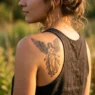 Woman with detailed angel tattoo on shoulder in golden sunlight showing intricate wing and figure details