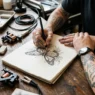 Tattoo artist's hand sketching custom butterfly design on paper with client's arm resting nearby