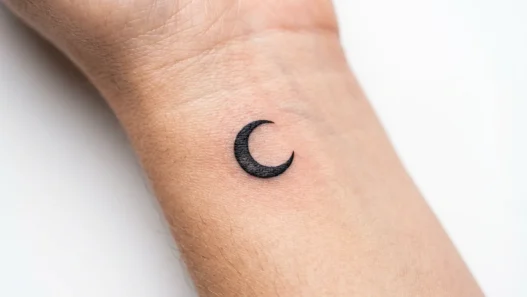 Tiny crescent moon tattoo on woman's inner wrist with clean black line work and precise details
