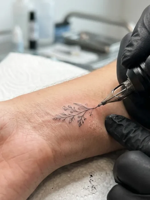 Close-up of tattoo needle creating fine lines on woman's wrist with bright studio lighting