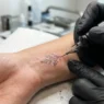Close-up of tattoo needle creating fine lines on woman's wrist with bright studio lighting