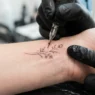 Single needle creating fine lines on woman's wrist during professional tattoo session with bright studio lighting