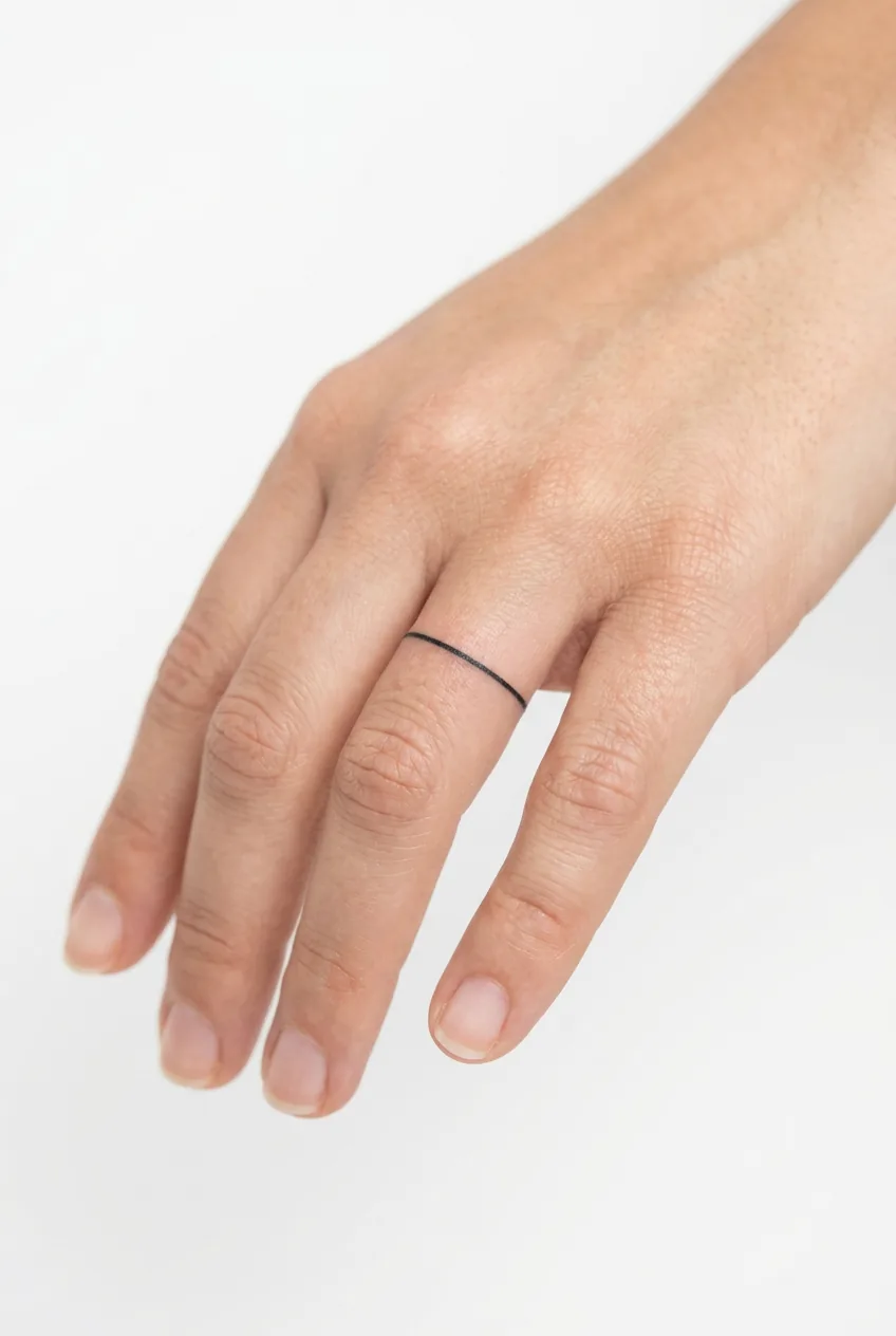 Simple black band tattoo on woman's ring finger showing clean line work