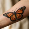 Close-up of detailed monarch butterfly tattoo on woman's forearm showing orange and black wing patterns