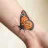 Detailed monarch butterfly tattoo on woman's wrist showing orange wings with black veining and white spots