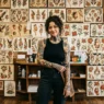 Woman with mythology tattoos standing in traditional tattoo studio with flash art wall background