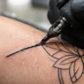Close-up of tattoo needle creating precise black lines on skin under bright clinical lighting