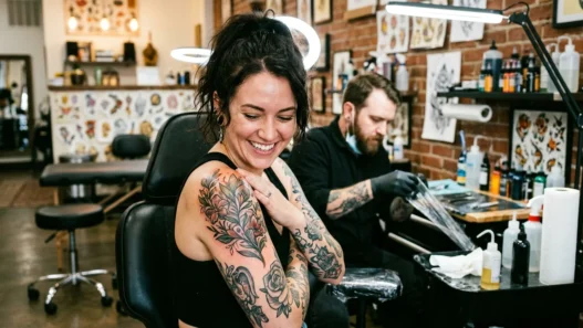 Woman looking down at fresh shoulder tattoo with delighted expression in bright tattoo studio