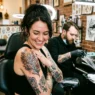 Woman looking down at fresh shoulder tattoo with delighted expression in bright tattoo studio