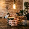 Woman with tattooed hands wrapped around ceramic coffee cup in trendy cafe with warm lighting