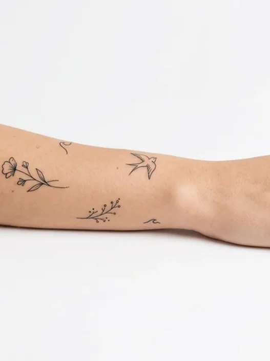 Collection of various tiny minimalist tattoos displayed on clean white background with studio lighting