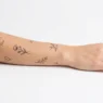 Collection of various tiny minimalist tattoos displayed on clean white background with studio lighting