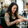 Woman in tattoo studio looking down at fresh shoulder tattoo with genuine delighted expression