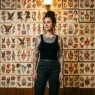 Woman with tattoos standing in front of traditional flash art wall in authentic tattoo studio