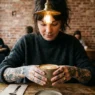 Woman with tattooed hands holding ceramic coffee cup in trendy cafe with exposed brick wall