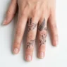Overhead close-up of a woman's hand showing multiple delicate fine-line botanical finger tattoos in bright studio lighting