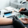 Tattoo artist preparing a single needle for fine-line work with machine resting on sterile tray in bright studio