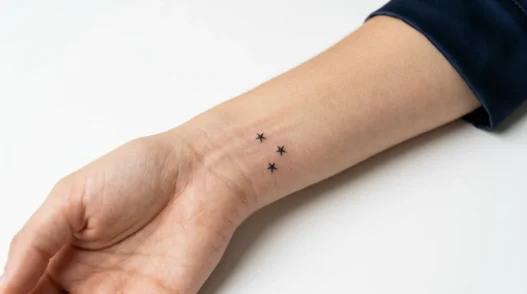 Woman's inner wrist displaying three tiny star tattoos arranged in constellation pattern with fine line black ink