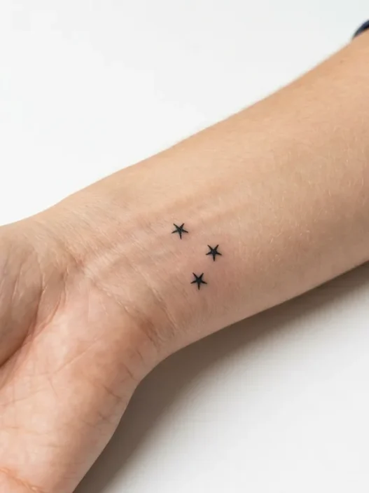 Woman's inner wrist displaying three tiny star tattoos arranged in constellation pattern with fine line black ink
