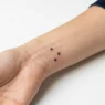 Woman's inner wrist displaying three tiny star tattoos arranged in constellation pattern with fine line black ink
