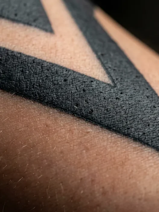 Extreme macro view of bold black and grey tattoo tonal range on a woman's forearm in soft studio lighting