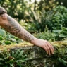 Woman's forearm covered in fine illustrative botanical tattoos resting among ferns and foliage in a botanical garden