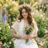 Woman with fine-line floral tattoos and a wildflower crown standing in a blooming garden in soft golden light