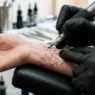 Close-up of tattoo needle creating fine lines on woman's wrist with bright studio lighting