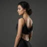 Woman standing in profile showing an elegant lower back tattoo in neutral studio lighting with grey background