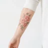 Woman's inner forearm with blush pastel peony cluster tattoo displayed on white studio backdrop in editorial lighting