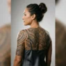 Woman in side profile showing a full Polynesian tribal back tattoo under professional rim lighting on grey background
