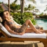 Tattooed woman reclining on pool lounger in bikini with ribcage and thigh tattoos visible in afternoon resort sun