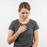 Woman in studio touching her sternum thoughtfully, demonstrating chest tattoo placement awareness
