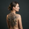 Woman showing large custom illustrative upper back tattoo spanning both shoulder blades in editorial studio lighting