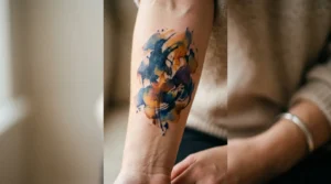 Woman's inner forearm with loose watercolor abstract tattoo in navy and amber ink tones under soft studio lighting
