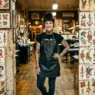 Tattooed woman standing before a wall of traditional flash art sheets under warm studio lighting